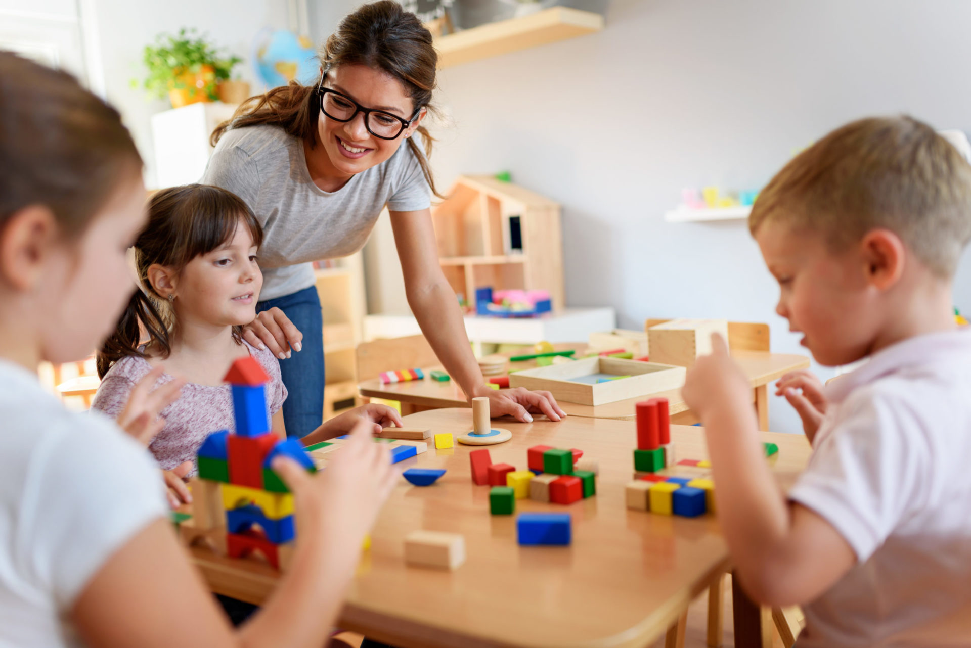 Preschool teacher with children playing with colorful wooden blocks